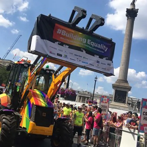 A pride parade with a colourful tractor displaying a rainbow flag that reads 'Building Equality'